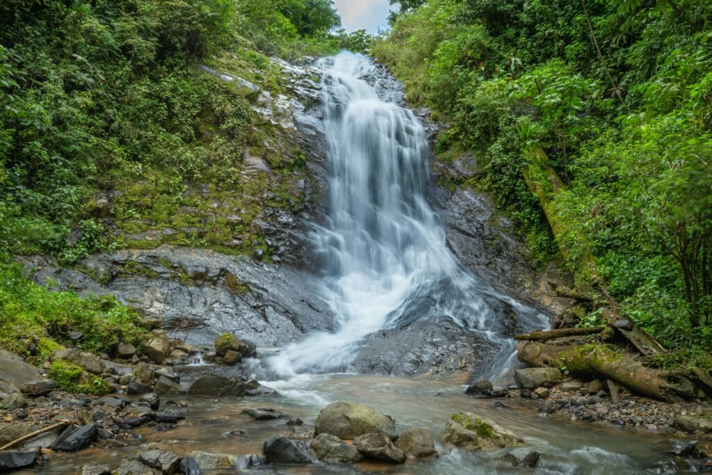 Wide waterfall flowing down a rocky slope into a shallow pool surrounded by tropical jungle foliage on an overcast day in Costa Rica