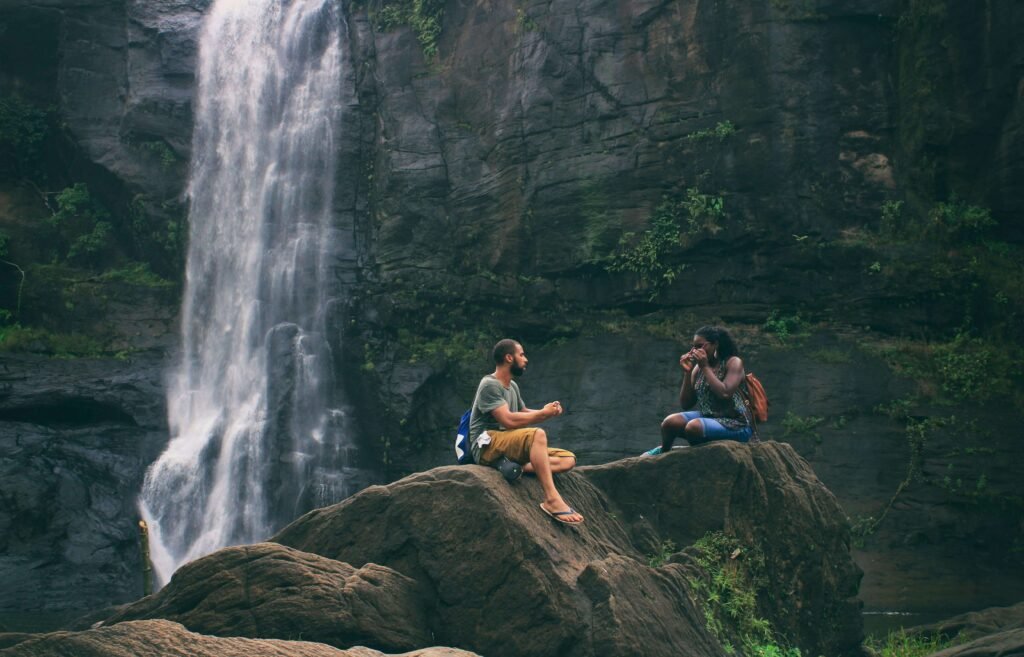 A couple relaxing on rocks beside a tropical waterfall, similar to the natural waterfalls near the thermal hot springs at Rincon Thermals and Adventures in Guanacaste