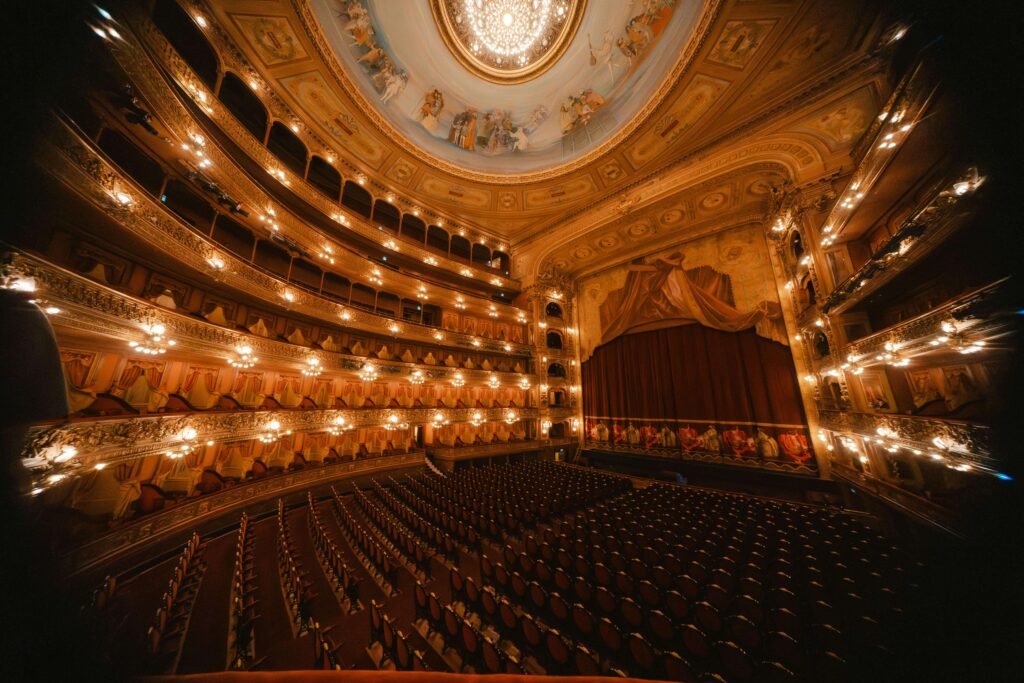 Grand interior of Teatro Nacional Costa Rica showing empty red velvet seats, multiple gilded balcony levels, chandeliers, and a painted ceiling dome