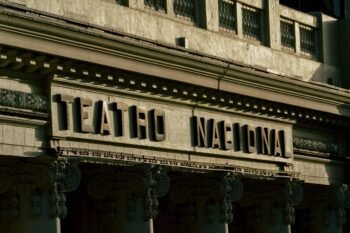 Close-up of the Teatro Nacional stone facade sign in San José, Costa Rica, with ornate Corinthian columns and carved architectural details in morning light