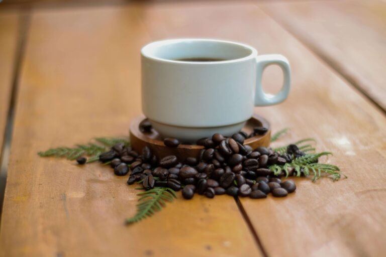 White ceramic cup of freshly brewed Costa Rican coffee surrounded by roasted coffee beans and green fern leaves on a wooden table at a coffee farm