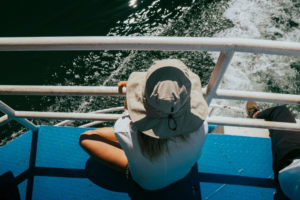 Traveler in a wide-brim sun hat sitting on the upper deck of the Puntarenas to Paquera ferry, looking out at the wake and open water of the Gulf of Nicoya