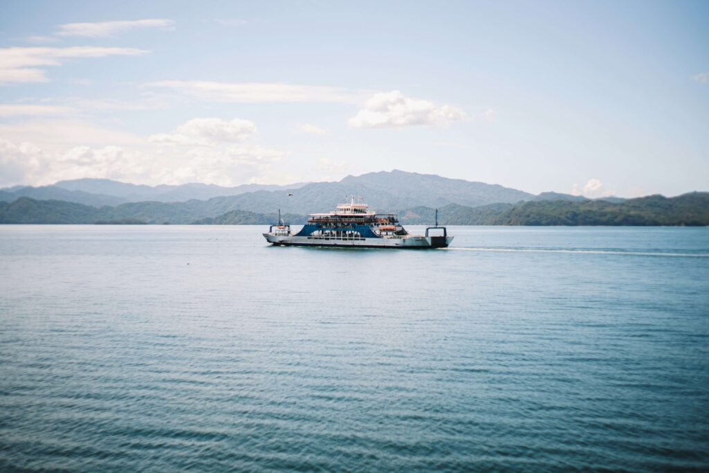The Puntarenas to Paquera car ferry crossing the calm blue waters of the Gulf of Nicoya, with green mountains of the Nicoya Peninsula visible in the background