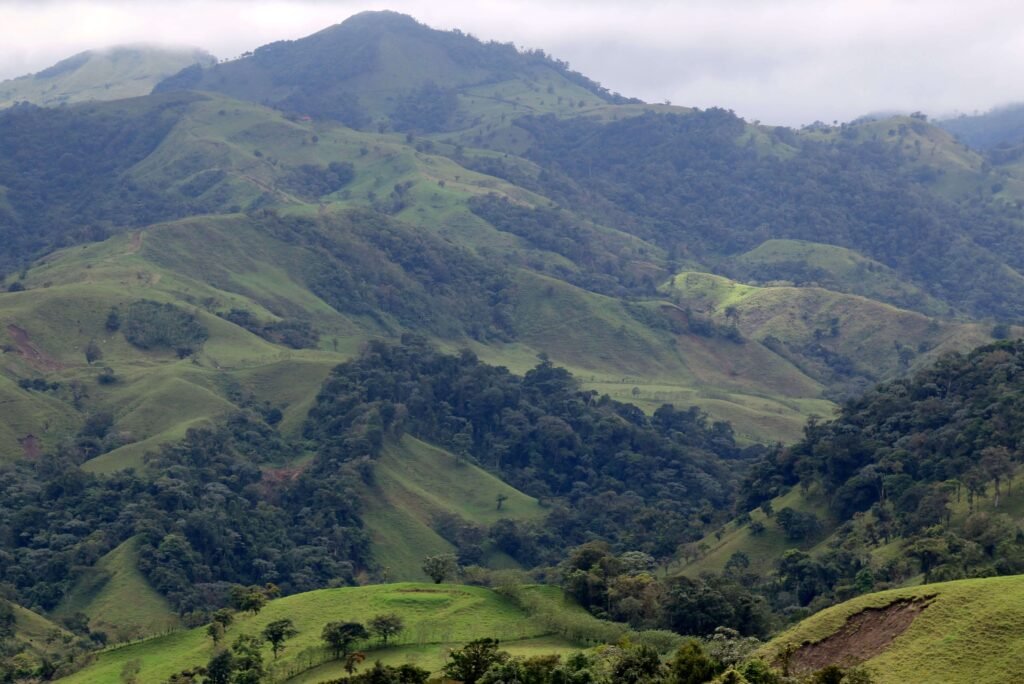 Rolling green hills and a cloud-topped mountain in the Orosi Valley, similar to the views from Hacienda Orosi