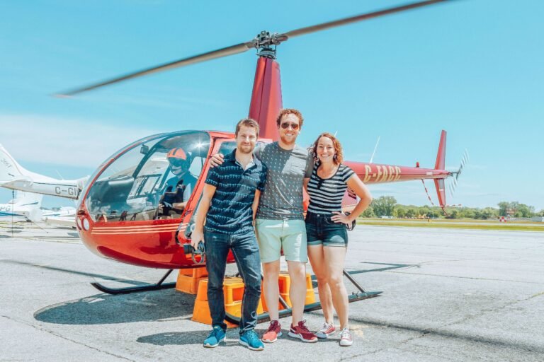 Three travelers posing beside a small red helicopter before takeoff, similar to a group helicopter tour in Costa Rica