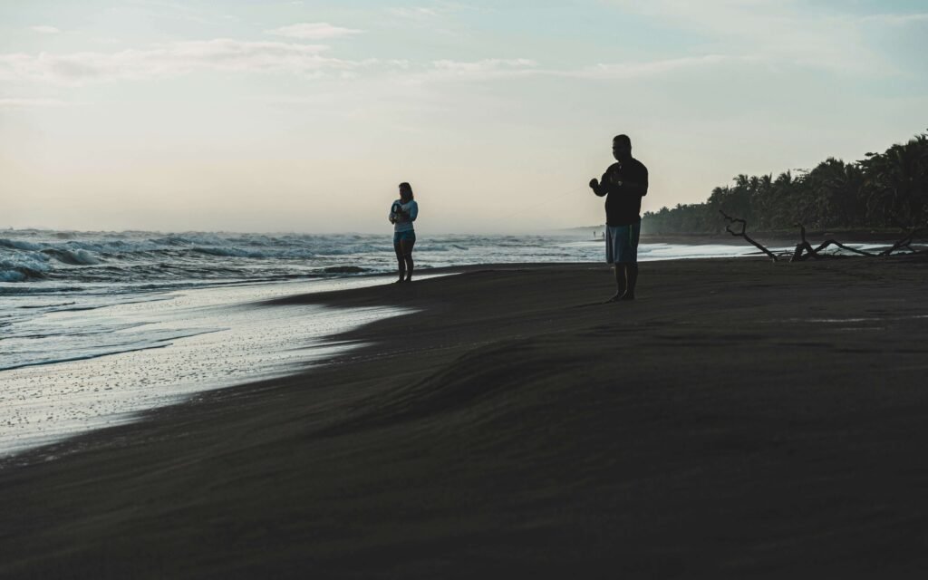 Two people standing on the beach near the waterline at dusk with palms along the shore, similar to Playa Cocles, Costa Rica