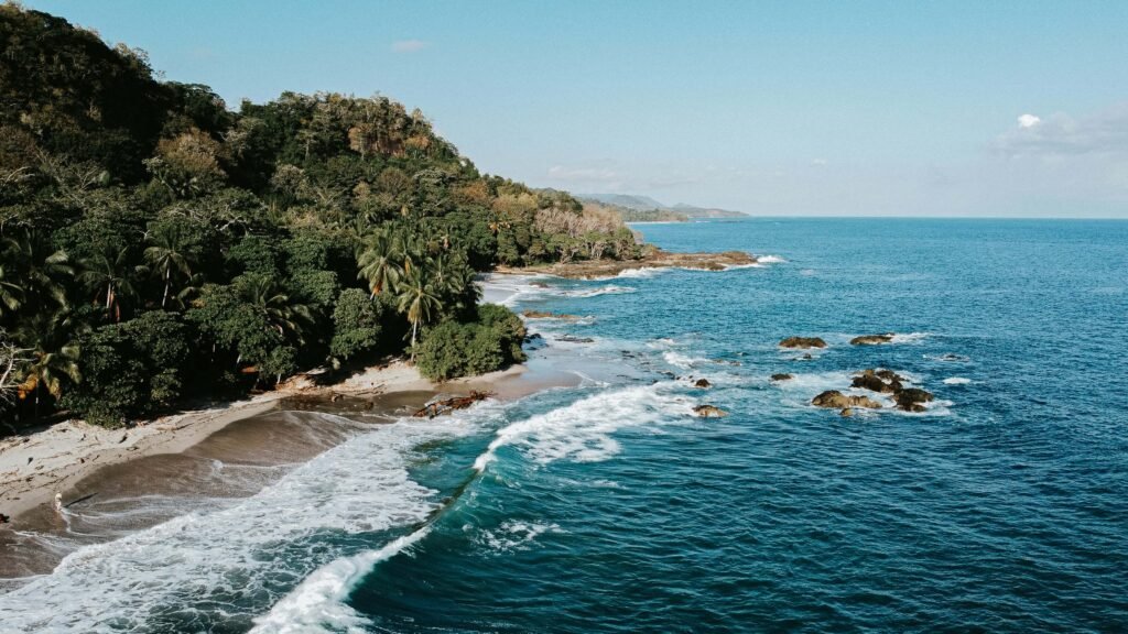 Aerial view of a jungle-backed beach with rocky shelves, similar to the Nicoya Peninsula coast near Playa Cocolito, Costa Rica