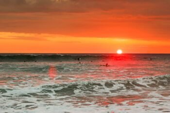 Surfers waiting in the lineup as the sun sets over the Pacific, similar to an evening surf session at Playa Grande, Costa Rica