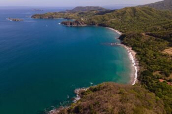 Aerial view of a turquoise cove and dry-forest hills along the Gulf of Papagayo, similar to Playa Iguanita, Costa Rica