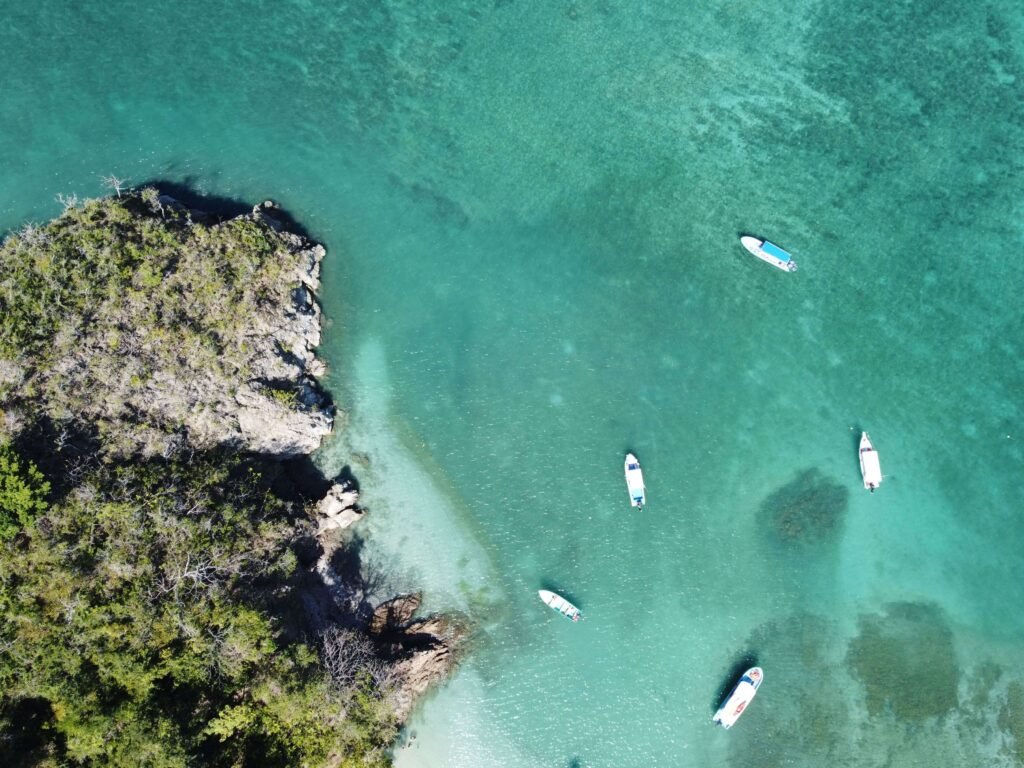 Aerial view of small boats anchored in clear turquoise water beside a rocky point, similar to San Juanillo bay, Costa Rica