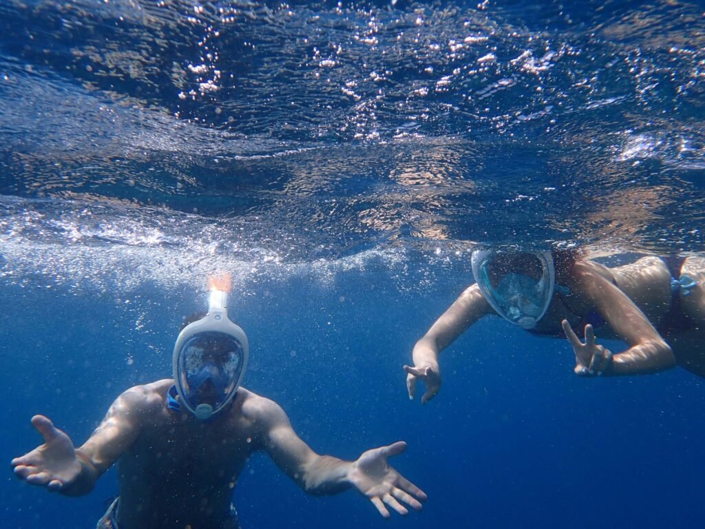 Two snorkelers in full-face masks at the surface in clear blue water, similar to snorkeling at San Juanillo, Costa Rica