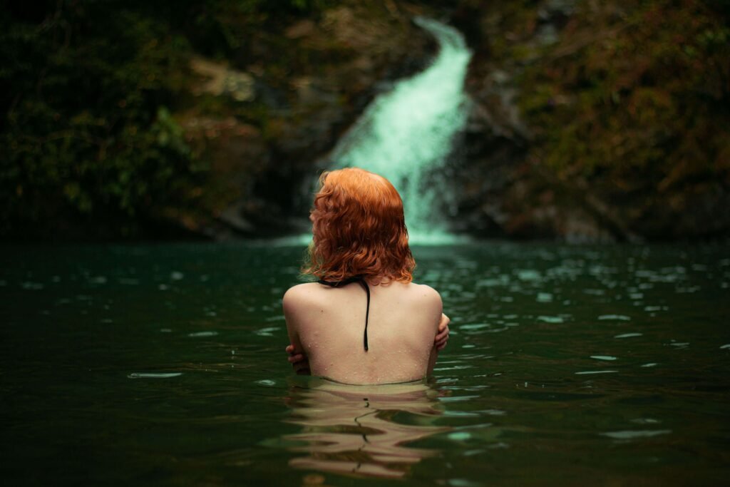 Swimmer in an emerald pool below a small jungle waterfall, similar to the swimming holes at Uvita Waterfall, Costa Rica